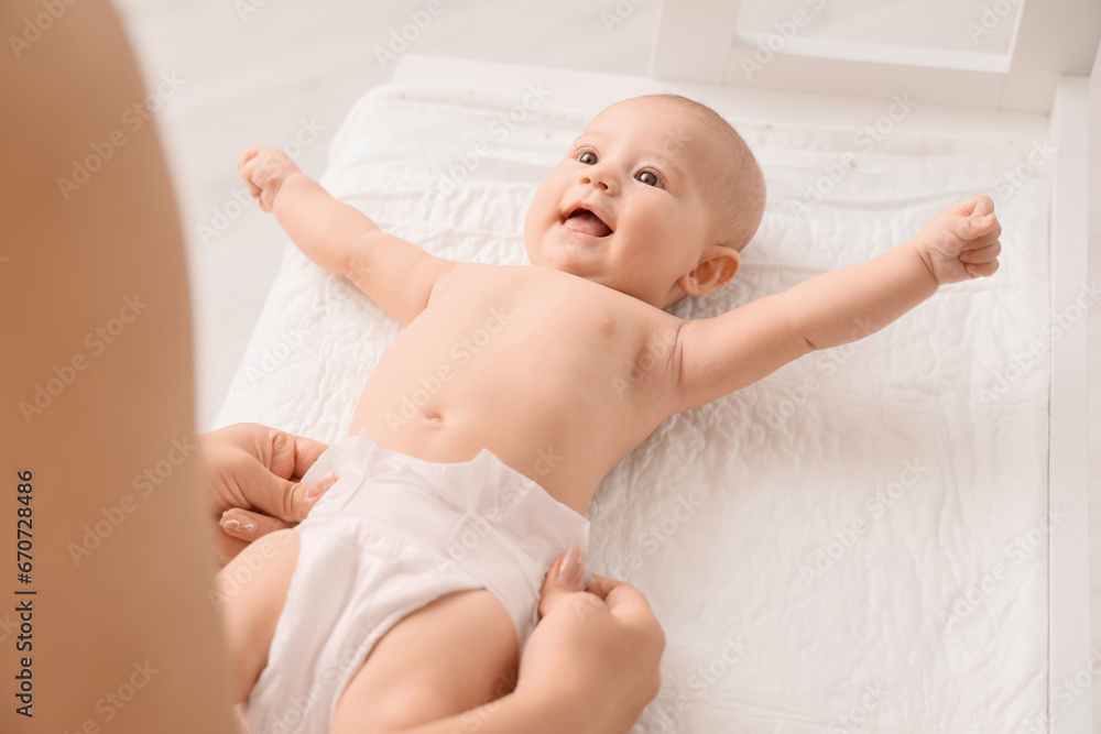 Mother putting diaper on her cute little baby at changing table