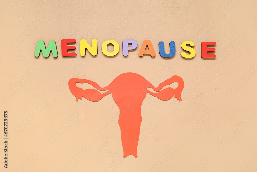 Word MENOPAUSE with paper uterus on beige background