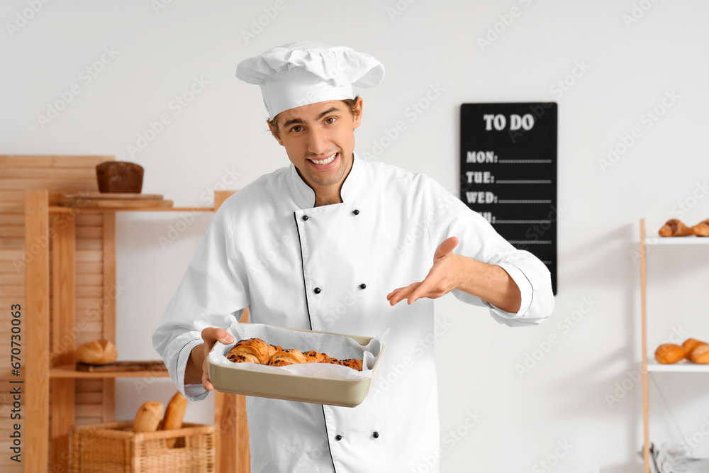 Handsome young chef holding baking dish with fresh croissants in bakery