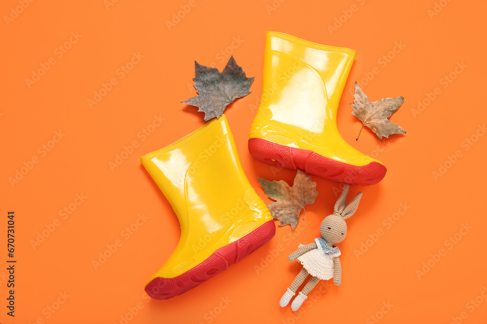 Yellow gumboots with toy bunny and autumn leaves on orange background