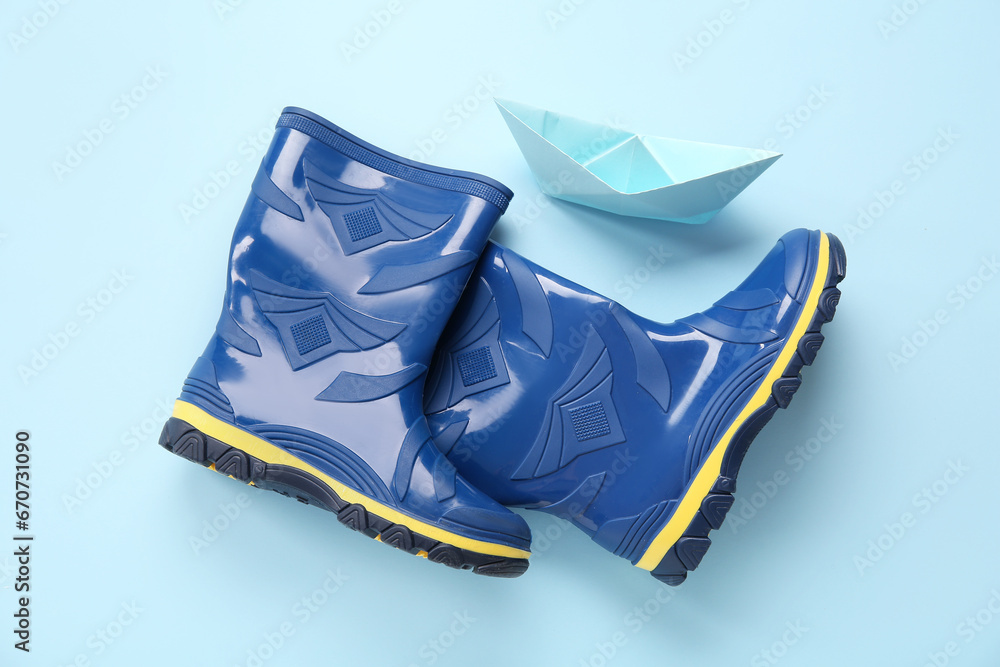 Blue gumboots and paper ship on color background