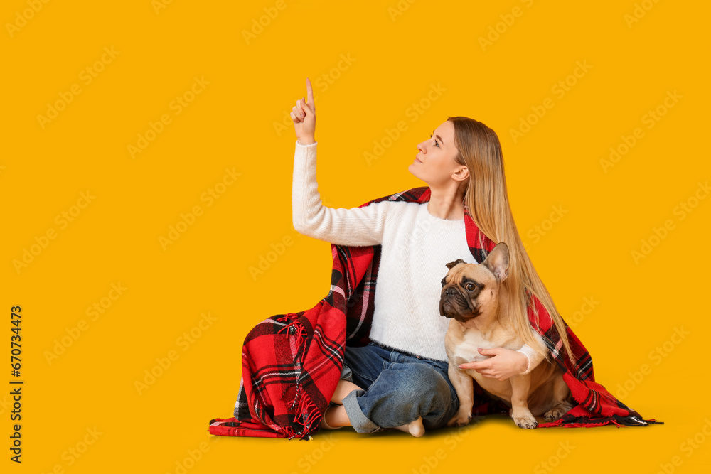 Beautiful young woman with cute pug dog and plaid pointing at something on yellow background