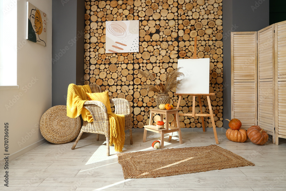 Interior of cozy living room with wicker armchair, easel and pumpkins