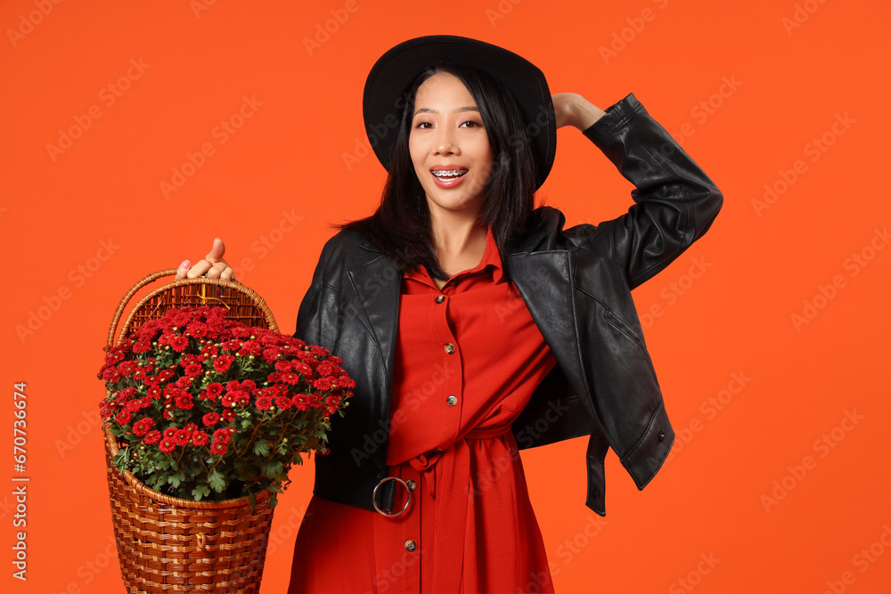 Young Asian woman with chrysanthemum flowers on orange background