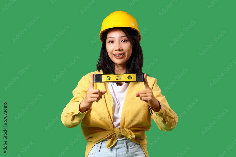 Young Asian woman with building level on green background