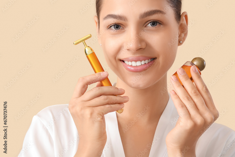 Beautiful young woman with facial massage tool and oil on beige background, closeup