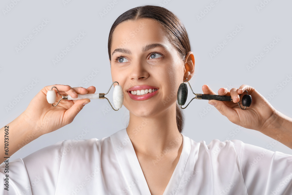 Beautiful young woman with facial massage tools on light background, closeup