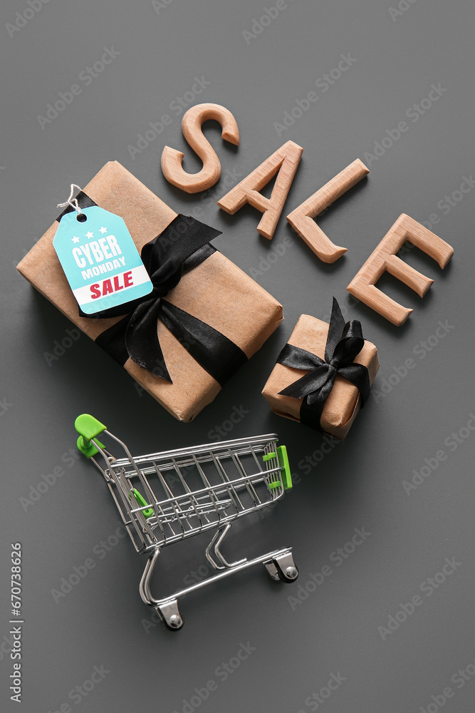 Composition with small shopping cart, gift boxes and word SALE on grey background. Cyber Monday