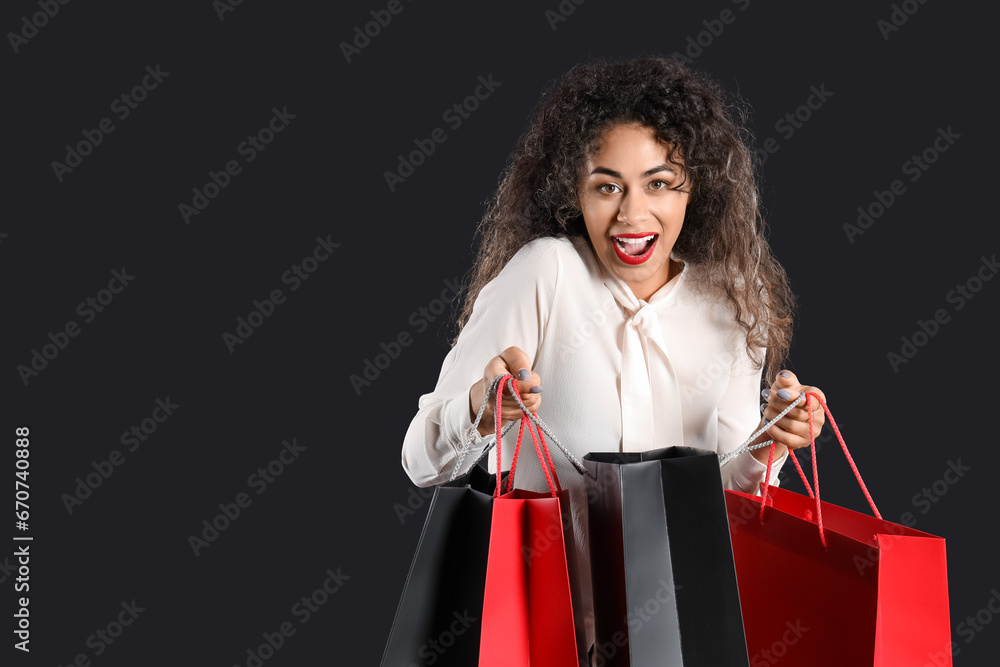 Beautiful African-American woman and shopping bags on dark background. Black Friday sale