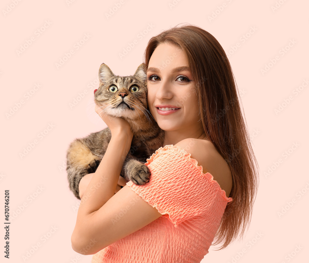 Pretty young woman with cute tabby cat on pink background