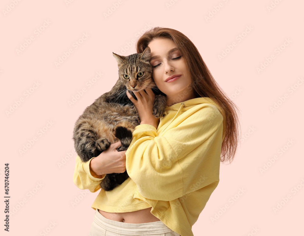 Pretty young woman with cute tabby cat on pink background