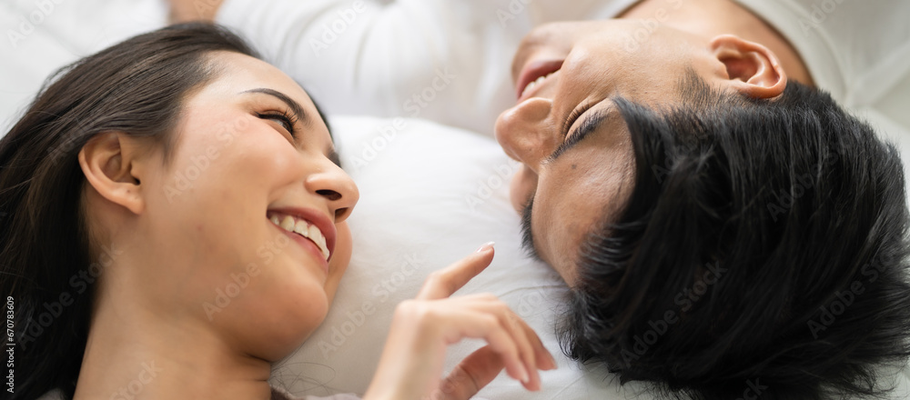 Asian new marriage couple lying down on bed and looking at each other. 