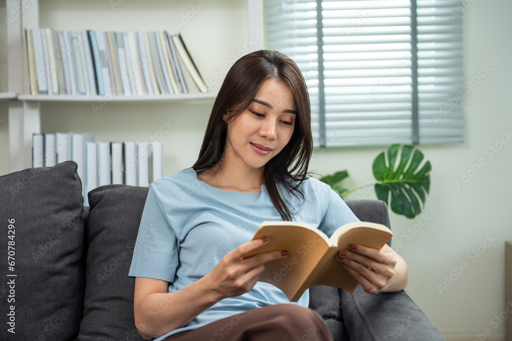 Asian young beautiful woman reading a book in living room at home. 