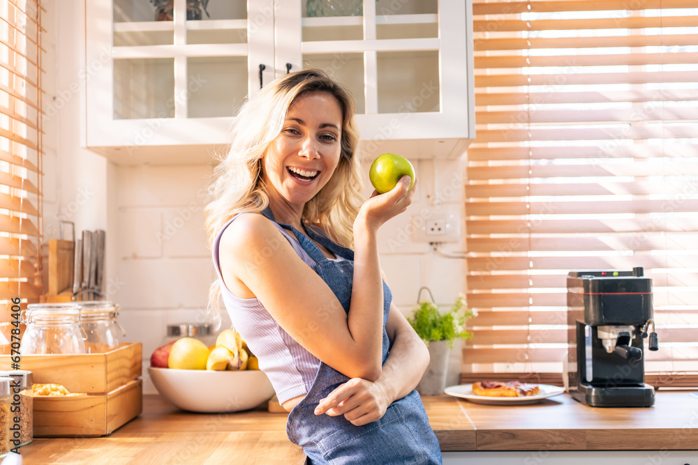 Caucasian young woman holding an apple on hands in the kitchen at home. 