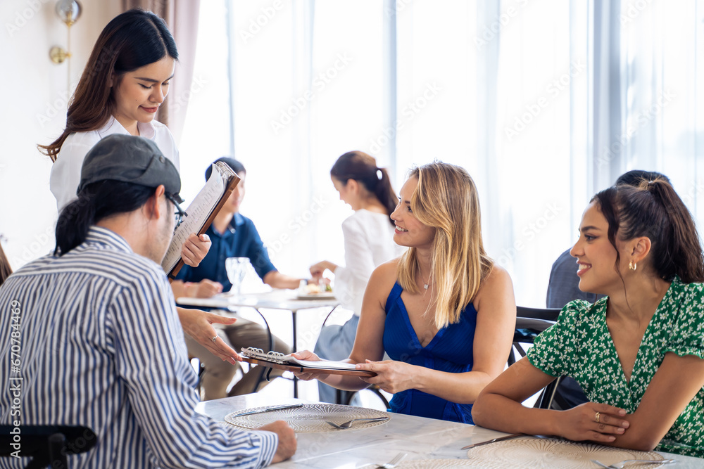 Asian waitress serving food to group of diverse customer in restaurant. 