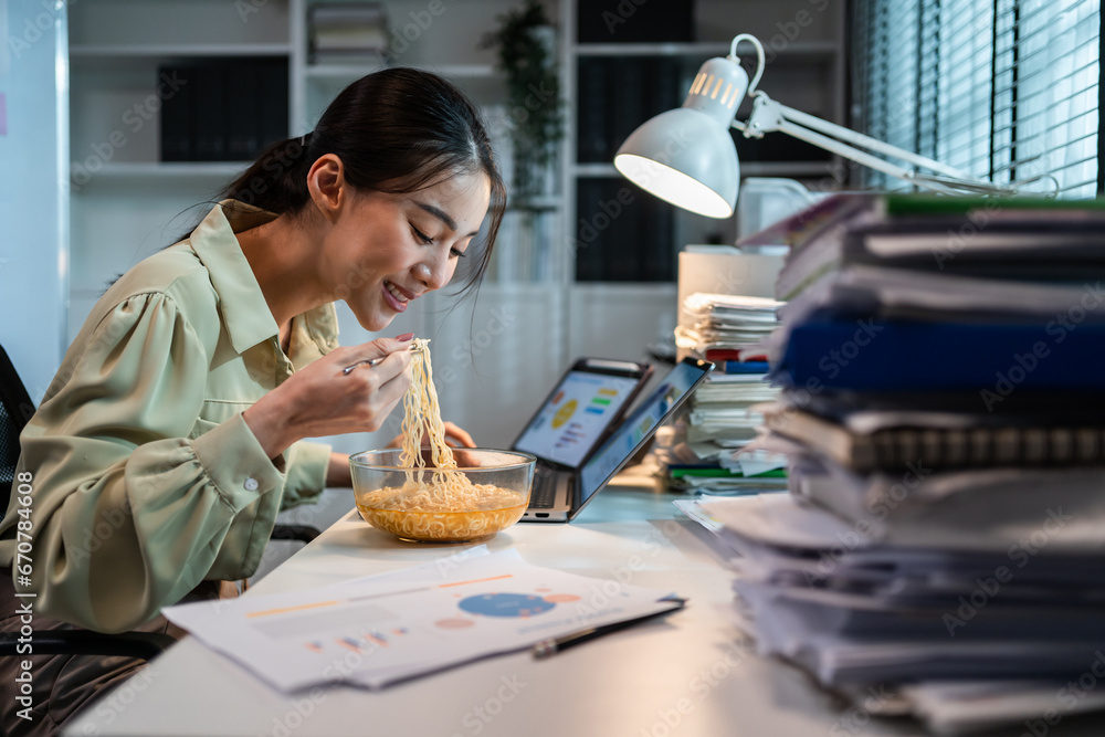 Asian young businesswoman eating noodles while work in office at night.