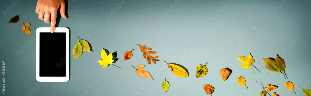 Autumn leaves with person using a tablet computer from above