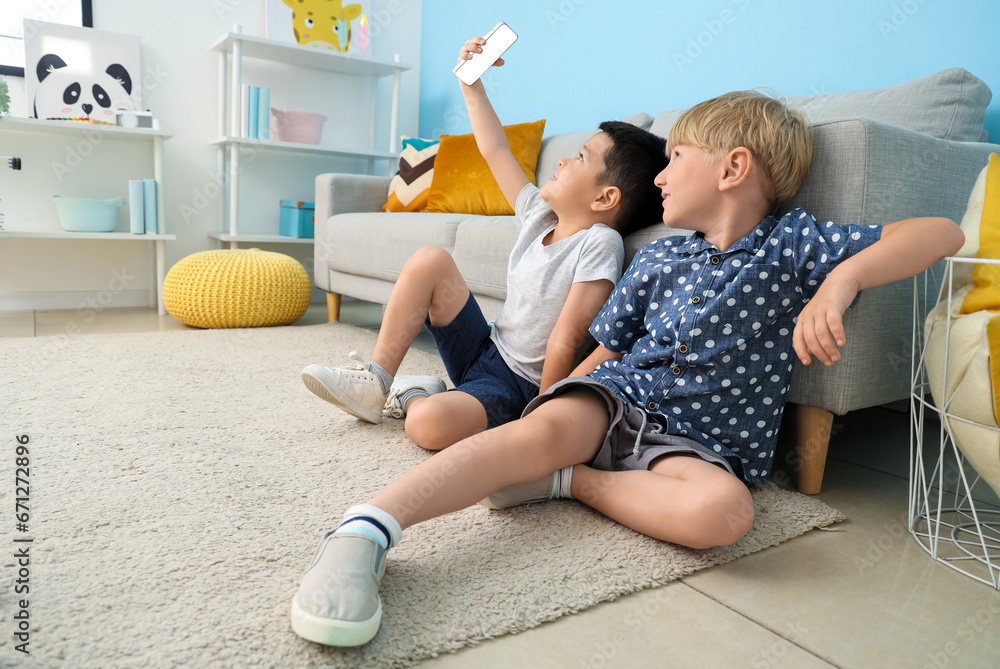 Cute little boys with mobile phone taking selfie at home