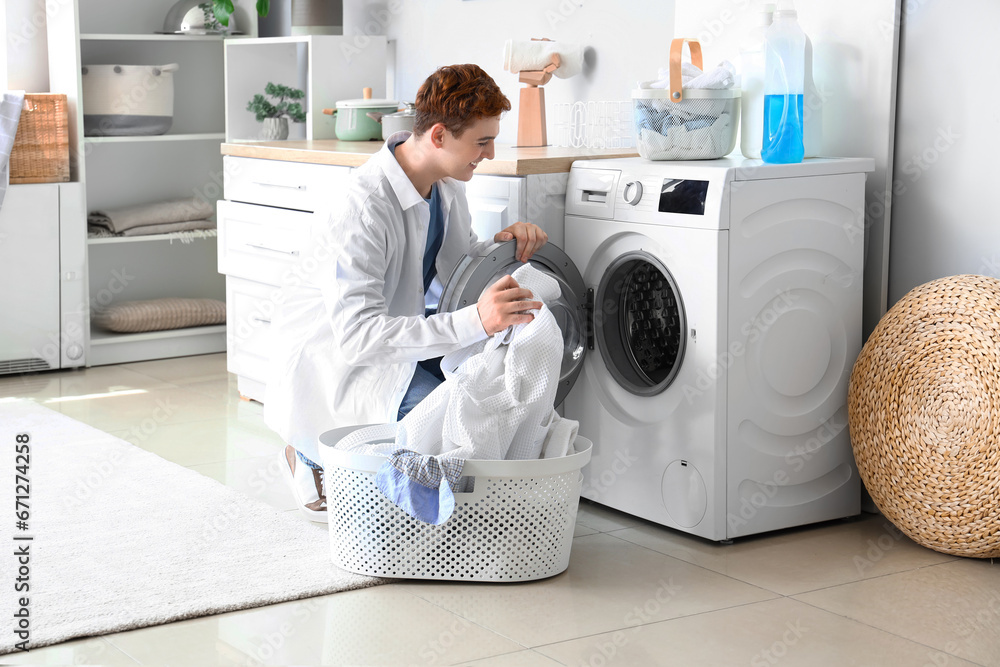 Young man putting laundry into washing machine at home