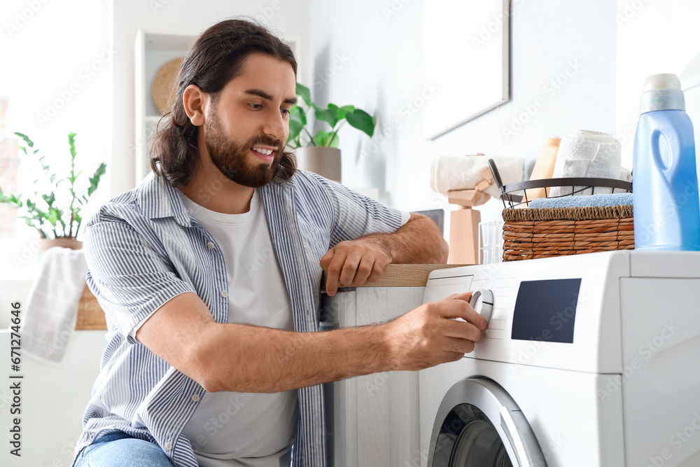 Young man switching on washing machine at home