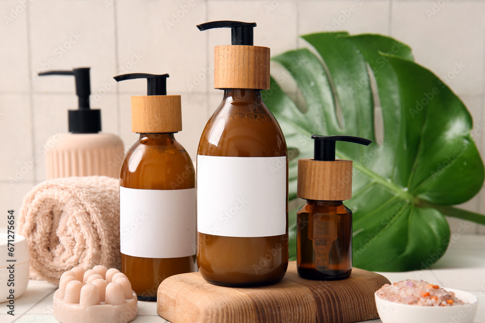 Bottles of shampoo and bath accessories on white tile background