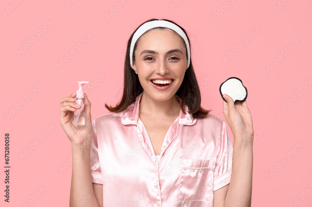 Young woman with reusable cotton pad and cleanser on pink background