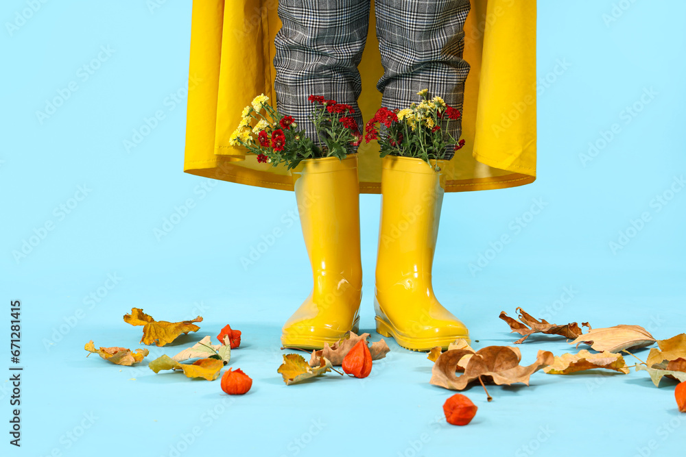 Young woman in gumboots with chrysanthemum flowers on blue background, closeup