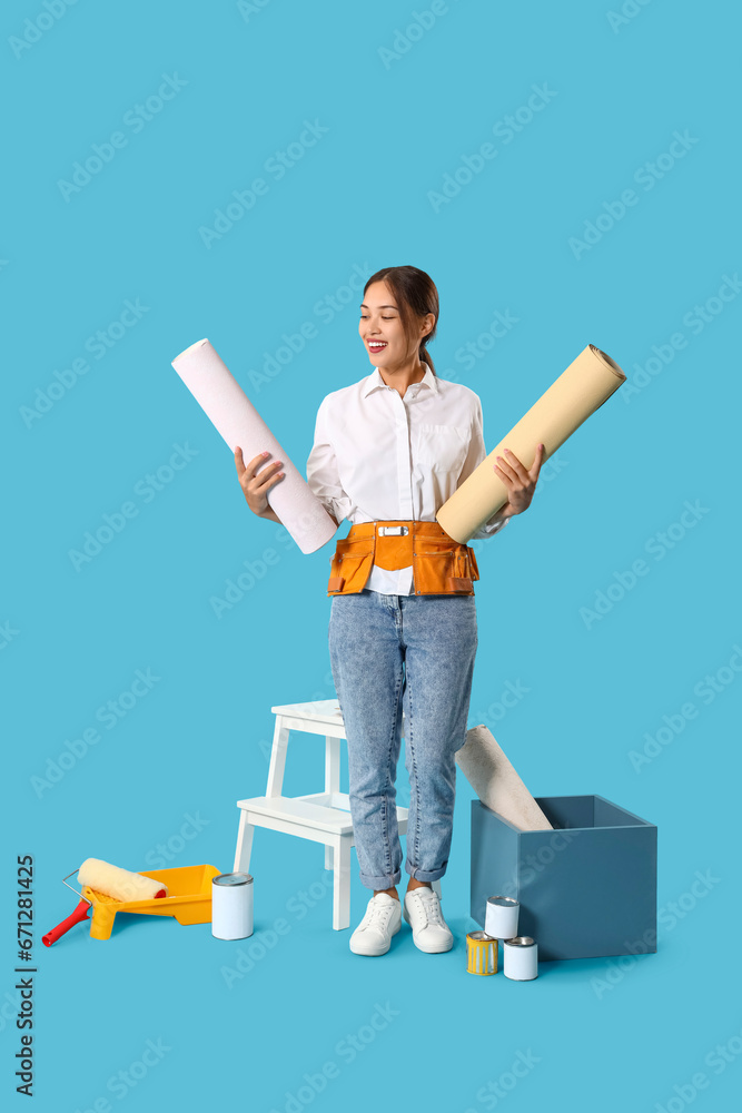 Female Asian decorator with wallpaper rolls on blue background