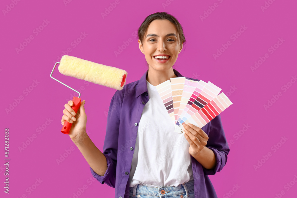 Young woman with paint color palettes and roller on purple background