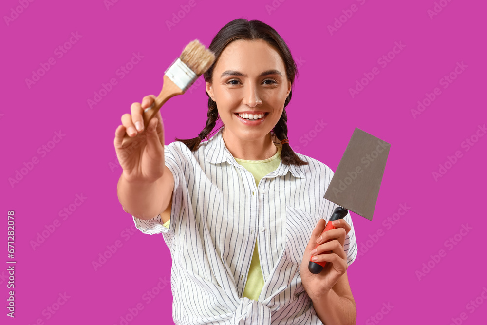 Young woman with paint brush and trowel on purple background