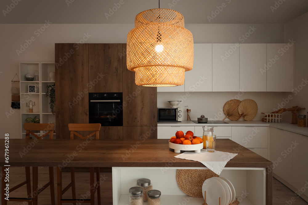 Interior of modern kitchen with wooden island table and glowing lamp