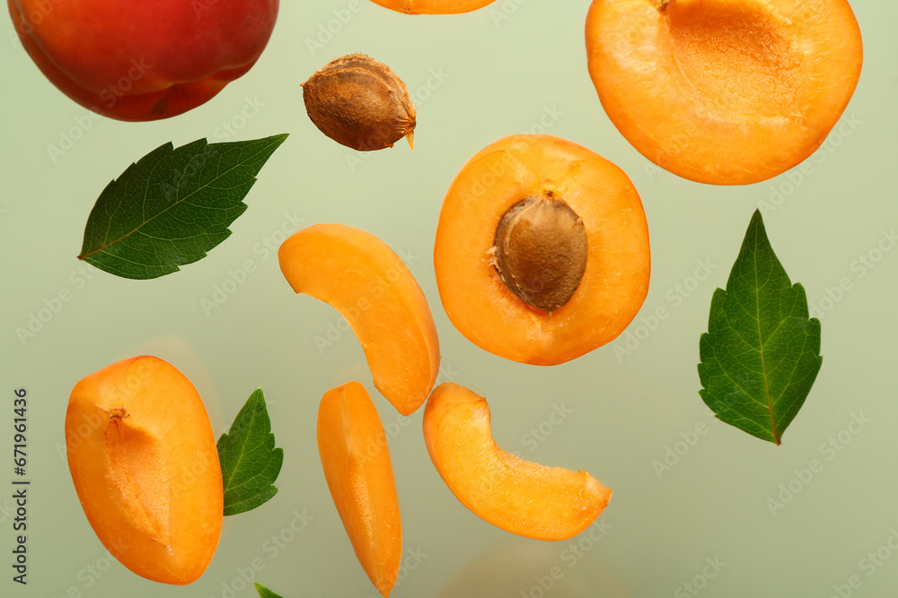 Flying halves of fresh apricot with pieces and leaves on green background