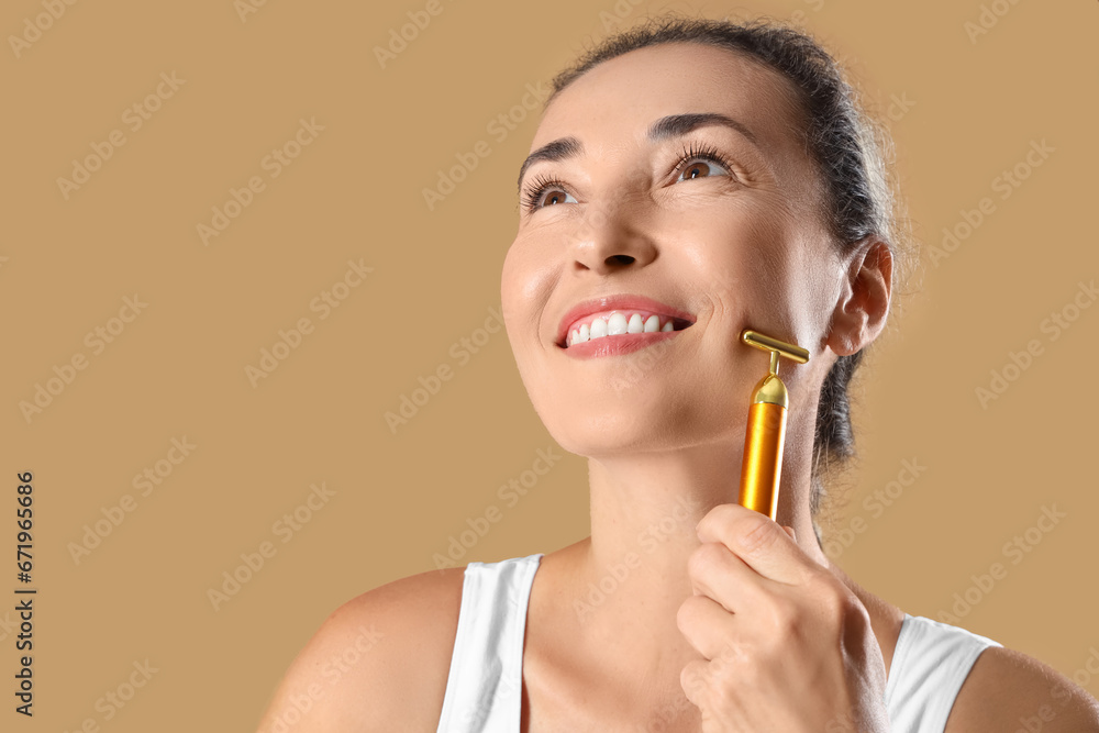 Beautiful mature woman with facial massage roller on beige background