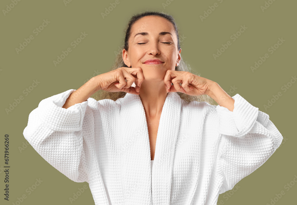 Beautiful mature woman giving herself face massage on khaki background