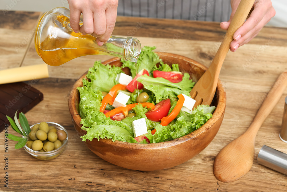 Woman adding olive oil into bowl with tasty salad at table