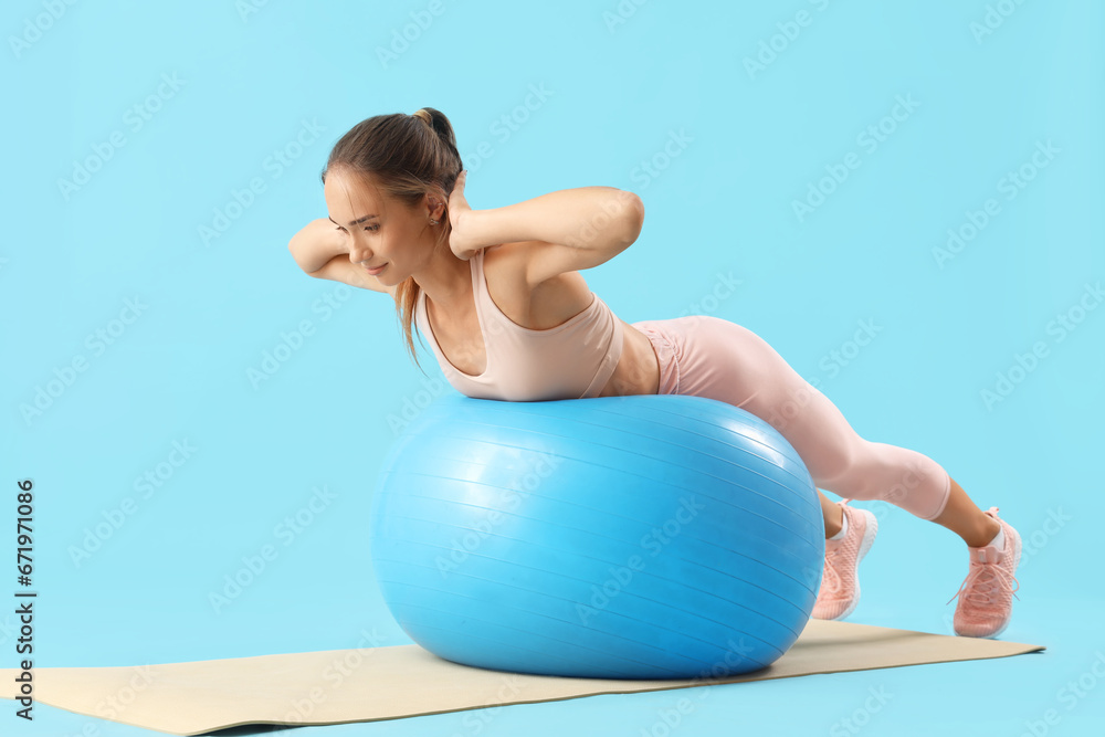 Sporty young woman with fitball training on blue background