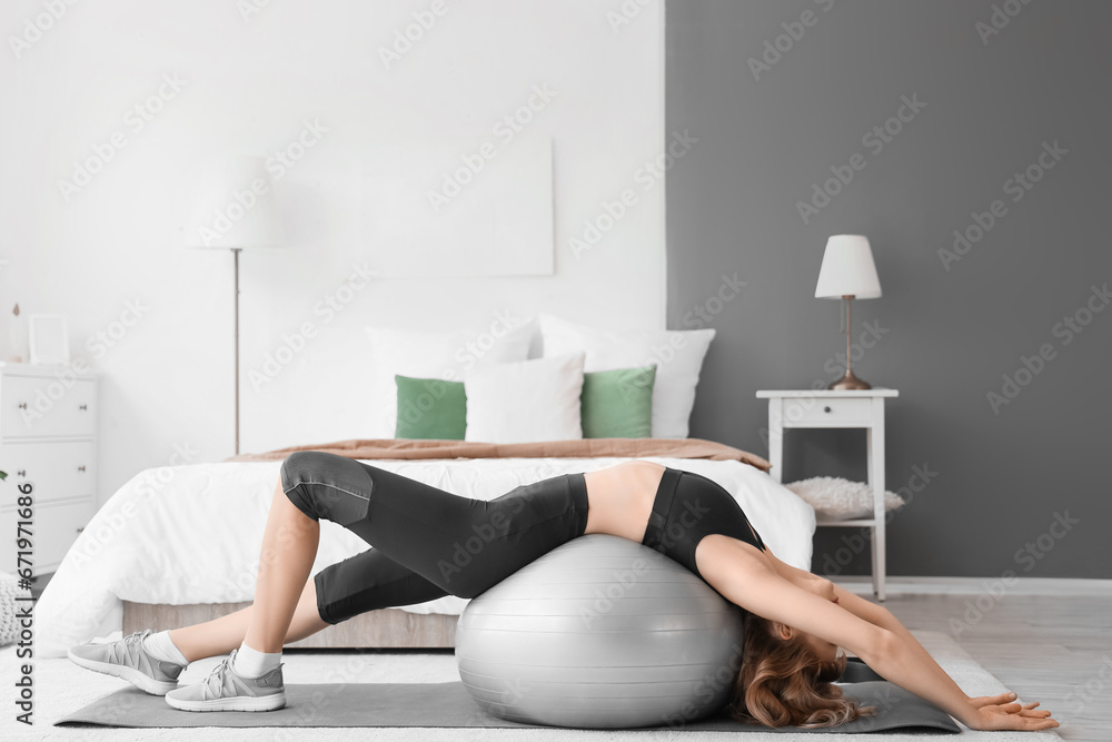 Young sporty woman stretching with fitness ball during training at home