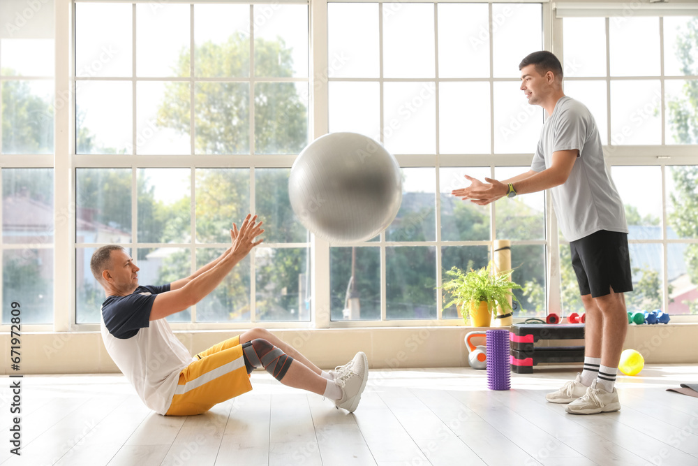 Mature man training with fitball and therapist in rehabilitation center