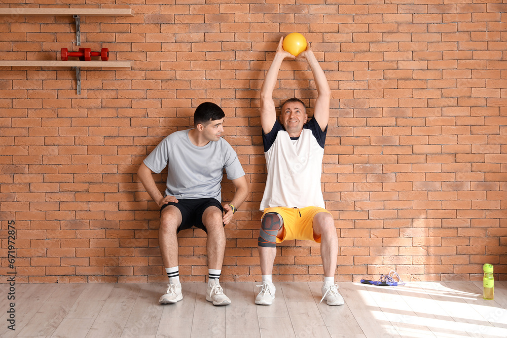 Mature man training with ball and therapist in rehabilitation center