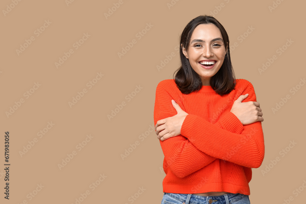 Young woman hugging herself on brown background