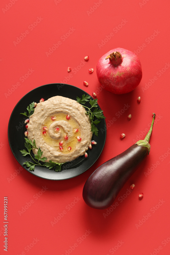 Plate of tasty baba ghanoush with eggplant and pomegranate on red background