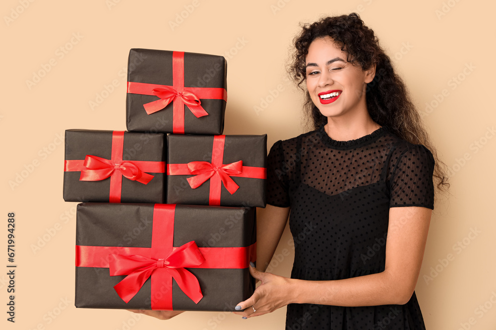 Beautiful African-American woman with gift boxes on beige background. Black Friday sale