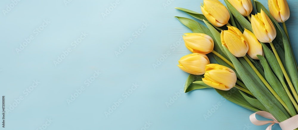 A photograph from a bird s eye perspective featuring a collection of yellow tulips arranged in a bouquet on a pastel blue fabric backdrop with a vacant area for additional elements