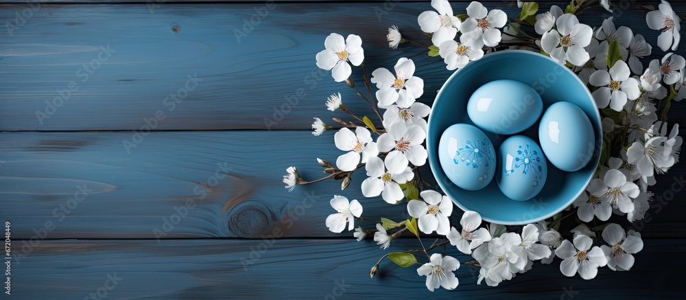 From an aerial perspective there is an assortment of Easter eggs colored with natural dyes resting on a blue dish The eggs are positioned amidst a bed of white flowers which adorn a white wo