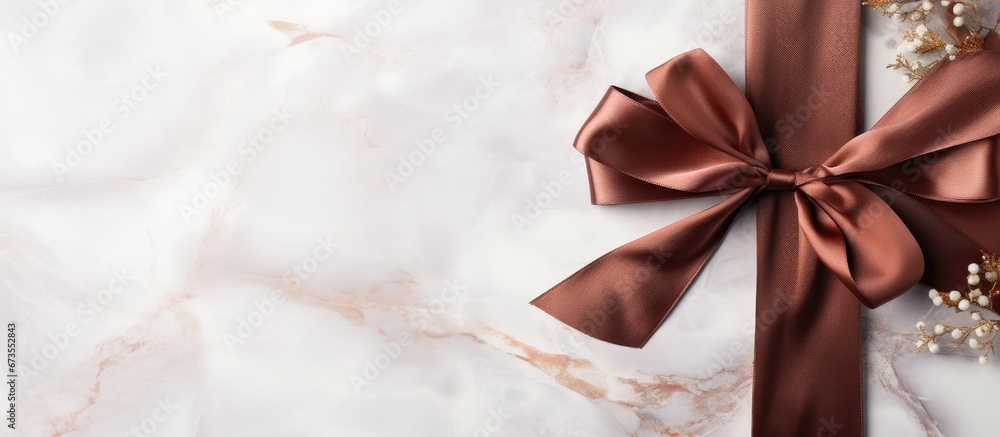 The concept of holiday gift decoration and sale promotion is represented by a flatlay of a chocolate brown silk ribbon on a marble background