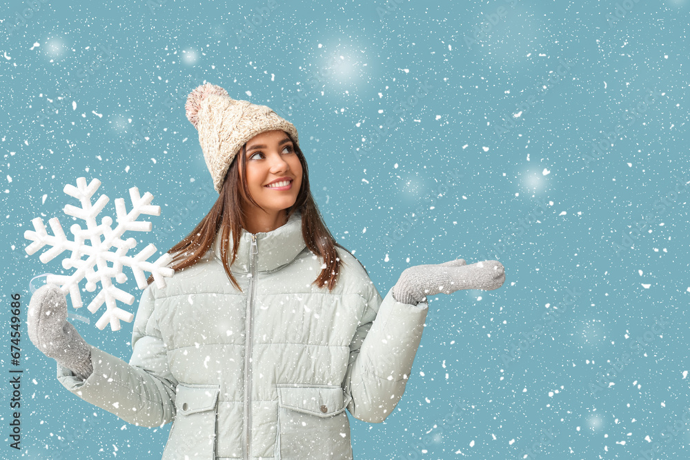 Beautiful woman in winter clothes holding big snowflake on light blue background