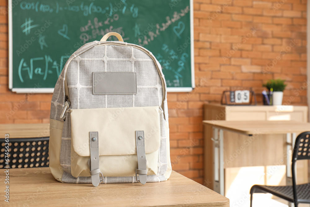 Stylish school backpack on desk in classroom