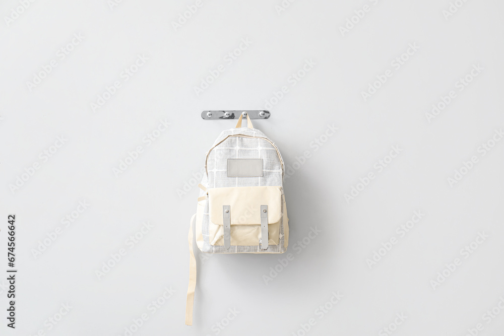 Stylish school backpack hanging on light wall