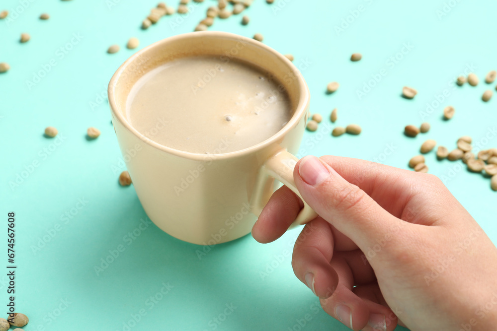 Woman holding cup of hot coffee on turquoise background