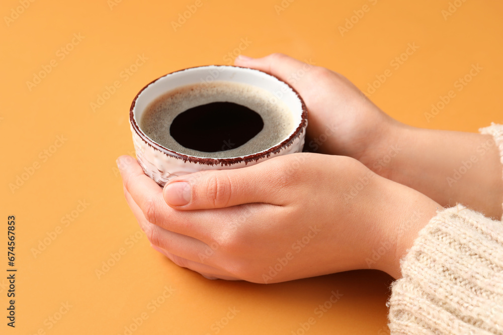 Woman holding cup of hot coffee on orange background